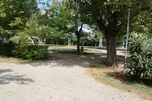 Schotterweg im Campinggelände mit Bäumen, grünen Büschen und Laternen entlang der Stellplätze.