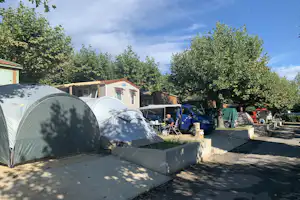 Camping International - Bick auf Mietunterkünfte teilweise im Halbschatten unter Bäumen mit Parkplatz und kleinem Zelt-Standplatz