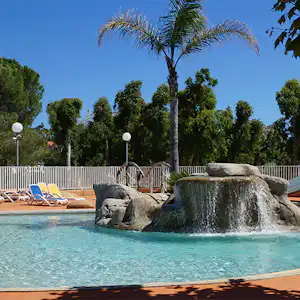 Camping-Pool mit Wasserspiel und Palmen, Liegen am Beckenrand und blauem Himmel im Hintergrund.