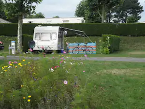 Wohnwagen auf dem Stellplatz mit Hecke, Blumenbeeten und Fahrrad vor dem Eingang, im Grünen am Campingplatz.