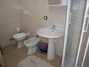 Badezimmer mit Waschbecken, Toilette und Dusche, gefliestem Boden und Wänden sowie Handtuchhalter im Hintergrund.
