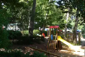 Spielplatz mit Rutsche und Klettergerüst im Grünen, umgeben von Bäumen und Hecken am Campingplatz.