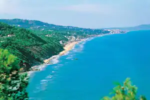 Blick auf die Küste mit langem Sandstrand, türkisfarbenem Meer und grünen Hügeln entlang der Bucht.