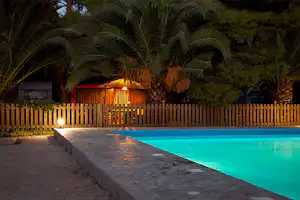 Camping Iria Beach - Pool vom Campingplatz am Abend mit Wohnwagen unter Palmen im Hintergrund