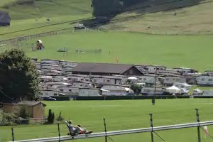 Wohnwagen und Campingfahrzeuge auf dem Campingplatz, Blick über grüne Hügel mit Zäunen und Spielplatz im Hintergrund.