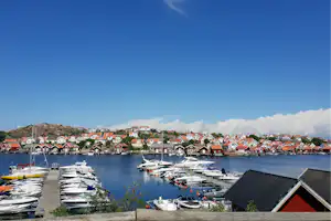 Hafen mit vielen Booten und Stegen, dahinter Häuser mit roten Dächern und ein Felsvorsprung am Ufer.