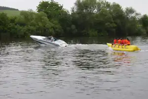 Ruderboot auf dem Fluss neben gelben Schlauchbooten mit Paddlern, umgeben von grünen Bäumen am Ufer.