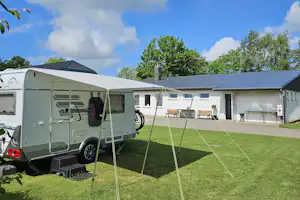 Wohnmobil mit Vorzelt auf einem Campingplatz, Rasenfläche und gepflasterter Weg vor einem Gebäude mit Fenstern.