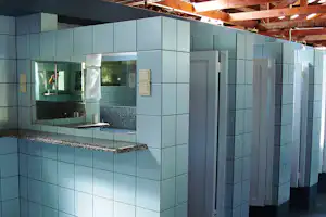 Weiße geflieste Küchenzeile mit Spüle und Arbeitsplatte, daneben Schranktüren und ein Fenster im Hintergrund.