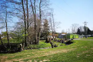 Bäume und grünes Gebäude auf dem Campingplatz, daneben Wohnwagen und Wege im Gras.