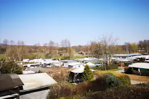 Campingplatz mit vielen weißen Zelten und Wohnwagen, umgeben von Bäumen und Wiesen im Tal unter klarem Himmel.