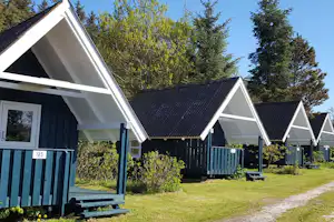Reihen von Ferienhäusern mit Holzveranda und blauem Zaun auf einer Rasenfläche, umgeben von Bäumen.