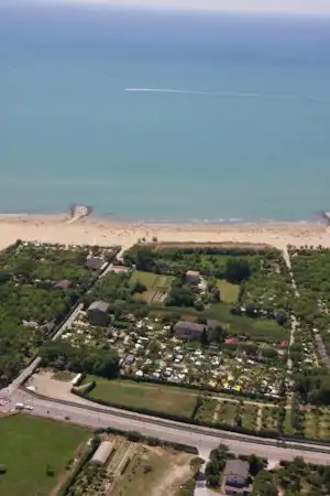 Luftaufnahme eines Campingplatzes nahe dem Meer mit Stellplätzen, Wegen, Grünflächen und einem Strandabschnitt am Ufer.