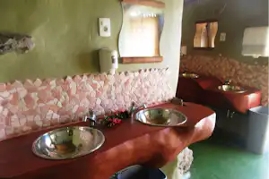 Zwei Waschbecken im Badezimmer mit Steinwand, Holzablage und Spiegeln, daneben eine grüne Duschwanne.