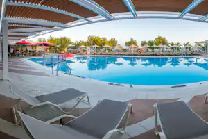 Schwimmbad mit blauem Wasser, Liegen auf der Terrasse, Sonnenschirmen und Reihen von Sonnenliegen unter einem Holzvordach.