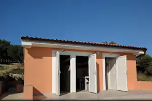 Bungalow mit Terrasse, offenen Türen und Fenstern unter blauem Himmel, gepflasterter Boden und Blick auf die Umgebung.