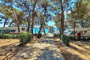 Campingplatzweg zwischen hohen Bäumen, Wohnwagen und Wohnmobilen, Blick auf das Meer durch die Bäume.