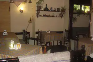 Innenbereich eines Camping-Restaurants mit mehreren Tischen, karierten Tischdecken, Kerzen und einer Bar mit Flaschenregal.