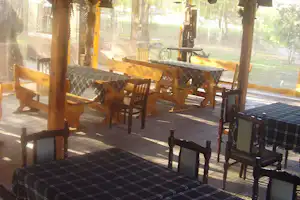 Holzterrasse mit Tischen und Stühlen, karierten Decken und Sichtschutz, im Hintergrund Bäume und warmes Licht.