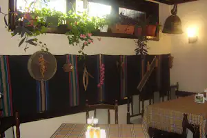 Gemütliche Camping-Ecke im Innenraum mit gestreiften Decken, Holzbänken, Tisch und hängender Deko aus Pflanzen und Laterne.