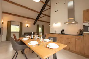 Essbereich mit Esstisch und Gläsern, daneben moderne Küchenzeile mit Kaffeemaschine und Dunstabzugshaube im Ferienhaus.