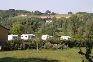 Wohnmobile und Caravans auf einem Campingplatz im Grünen, im Hintergrund Felder, Bäume und ein Landhaus.