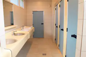 Camping-Badezimmer mit Waschbecken, Fliesenboden und Türen zu Duschkabinen, helles Interieur mit Wandfliesen.
