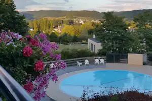 Blick auf den Pool und die Terrasse mit Gartenblumen, im Hintergrund Bungalows und grüne Hügel