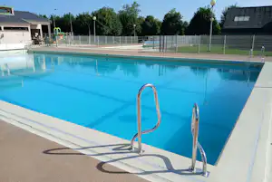 Schwimmbecken auf dem Campingplatz mit Leiter, Umrandung und Blick auf Zäune sowie Gebäude im Hintergrund.