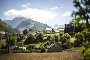 Blick auf ein Campingdorf mit kleinen Häusern und einem Holzschuppen, umgeben von grünen Wiesen und Bergen in der Ferne.
