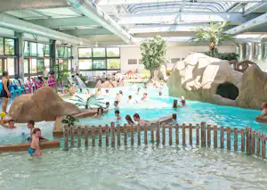 Überdachtes Hallenbad mit beheiztem Pool, großen Felsen und Glasdach; Kinder planschen im Wasser.