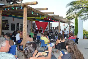 Musikgruppe auf der Camping-Terrasse unter Holzpergola mit Lichterkette, Gäste sitzen an Tischen und schauen zu.
