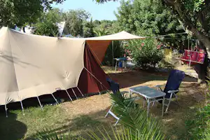 Großes Campingzelt im Garten mit Sonnenschirm, Tisch und Stühlen, umgeben von Bäumen und Sträuchern.