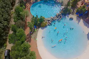 Blaue Außenpools im Campingplatz, umgeben von Palmen und Bäumen, mit Liegen und Wegen am Beckenrand.