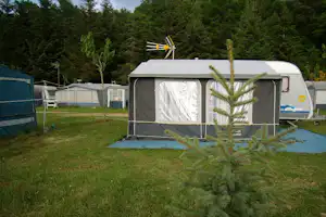 Wohnwagen mit Vorzelt auf einem Campingplatz, davor Rasen und junge Bäume, im Hintergrund weitere Zelte und Wohnwagen.