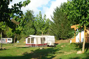 Wohnwagen mit Vorzelt auf dem Campingplatz, umgeben von Bäumen und grünem Rasen, im Hintergrund weitere Stellplätze.
