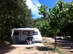 Wohnwagen mit Vorzelt und Sitzbereich am Campingplatz, umgeben von Bäumen und Rasenfläche.