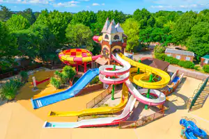 Wasserrutschen und Planschbecken auf einem Campingplatz, mit bunten Rutschen, Spielturm und Liegestühlen am Rand.