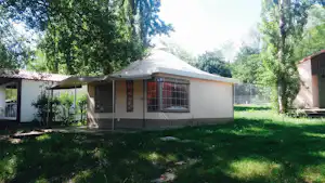 Bungalow im Grünen mit Rasenfläche, Hecke und Bäumen, daneben ein weiteres Gebäude am Campingplatz.