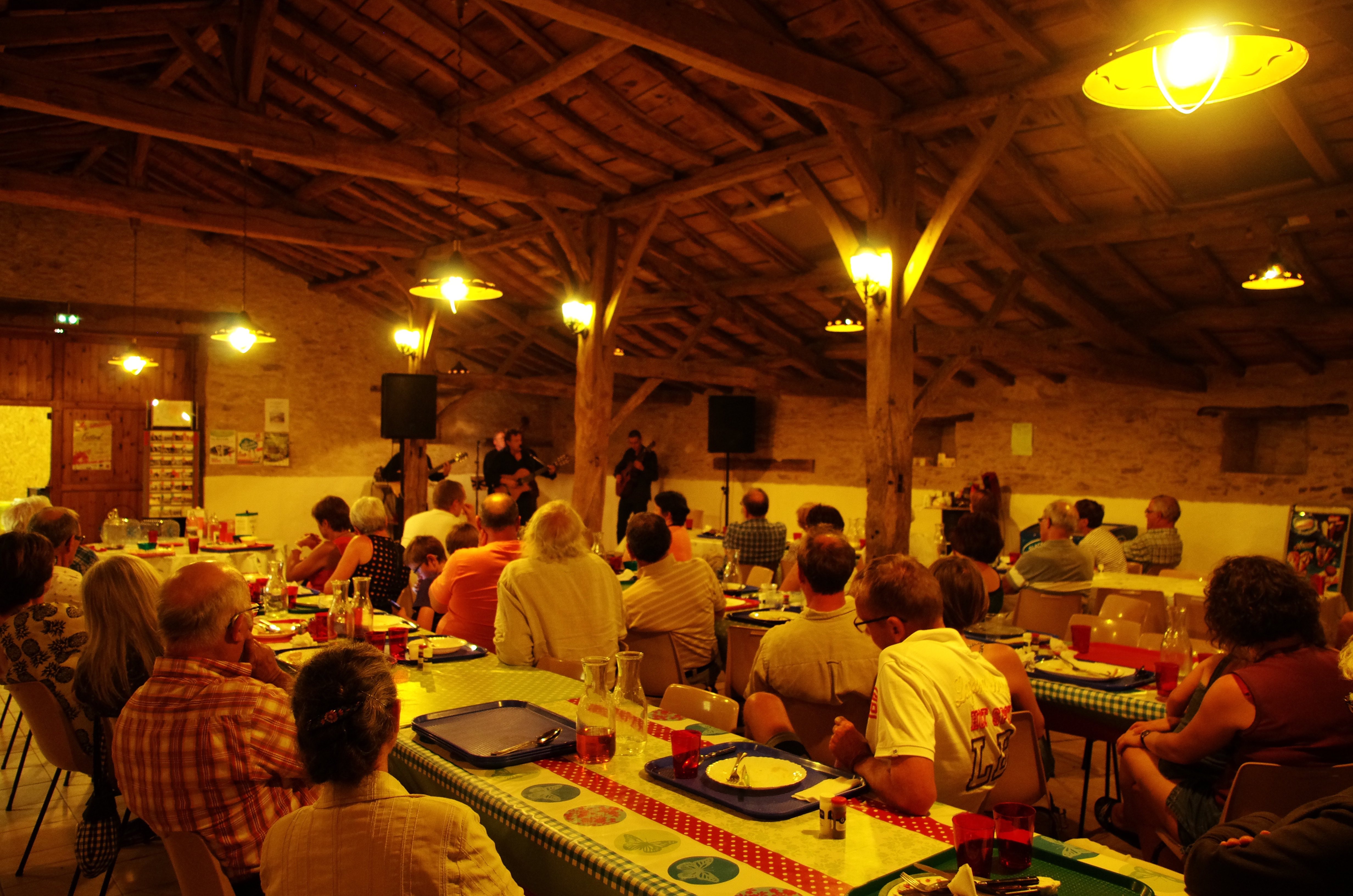 Innenraum eines Campingrestaurants mit Buffet und langen Tischen, viele Gäste sitzen beim Essen unter Holzdecken.