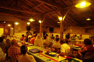 Innenraum eines Campingrestaurants mit Buffet und langen Tischen, viele Gäste sitzen beim Essen unter Holzdecken.