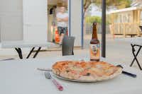 Camping La Bergerie Plage - Gedeckter Tisch mit Pizza und einer Flasche Bier-