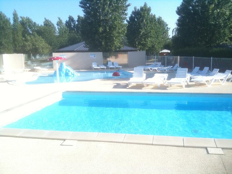 Campingpool mit blauem Wasser und mehreren Liegen am Beckenrand, dahinter Zaun und Bäume.