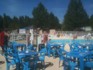 Blauer Stuhlbereich am Camping-Pool mit mehreren Liegen, Zaun und Bäumen im Hintergrund.