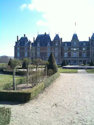 Schlossanlage mit Kiesweg, gepflegten Hecken und Bäumen im Garten vor dem großen Gebäude mit Türmen.