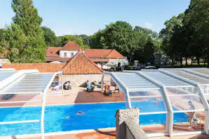 Beheizter Camping-Pool mit transparenter Überdachung, Steinmauer und Liegen auf der Terrasse vor einem Gebäude mit Ziegeldach.