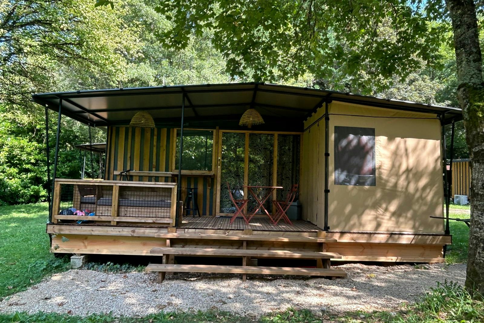 Mobilheim auf Holzterrasse mit Markise, davor Sitzgarnitur, umgeben von Bäumen und Rasen im Campingbereich.