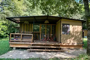 Mobilheim auf Holzterrasse mit Markise, davor Sitzgarnitur, umgeben von Bäumen und Rasen im Campingbereich.
