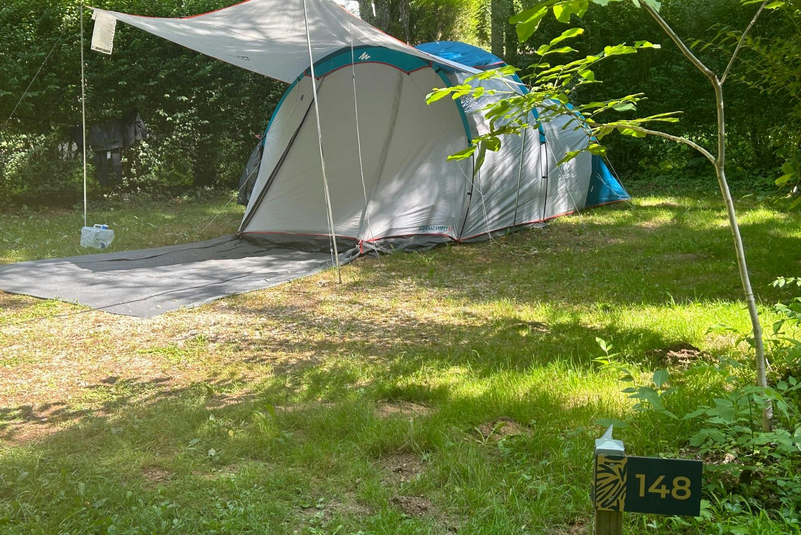Zelt auf einem Campingplatz im Grünen, mit Vorzelt und Stangen, auf einem gepflasterten Weg und Rasen.