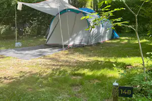 Zelt auf einem Campingplatz im Grünen, mit Vorzelt und Stangen, auf einem gepflasterten Weg und Rasen.